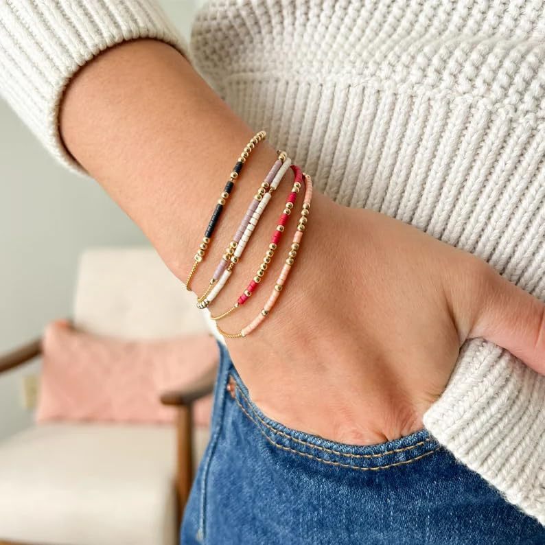 Woman wearing layered Morse Code bracelets in gold, pink, red, and black beads, representing hidden messages of love and strength.